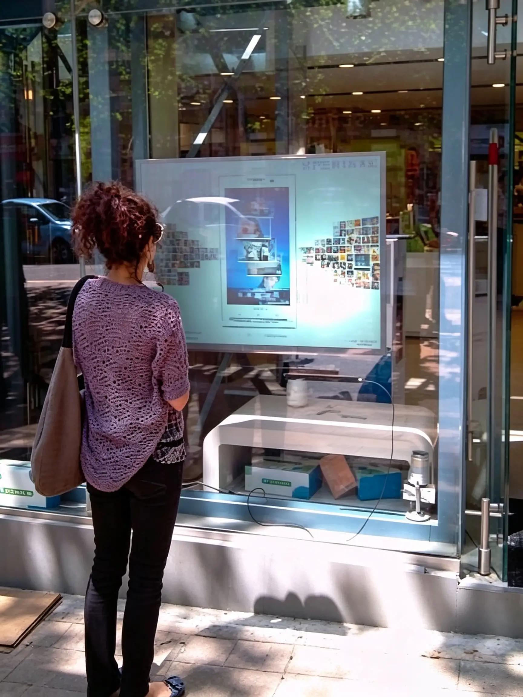 A modern retail storefront at night, glowing with a digital interactive product catalog visible through the glass window. A customer is touching the glass, interacting with the display. Sleek, high-tech, photorealistic.